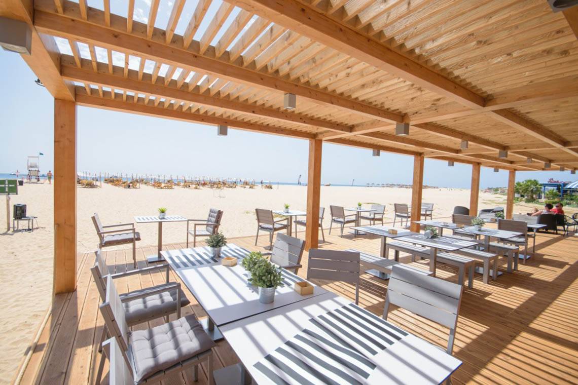 Außenterrasse des Oasis Salinas Sea Hotels mit Tischen und Stühlen auf einem hölzernen Boden.