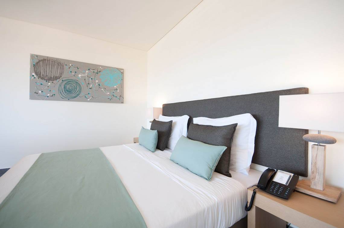 Ein stilvolles Hotelzimmer im Oasis Salinas Sea mit einem Doppelbett, Kissen, Telefon und Lampe.