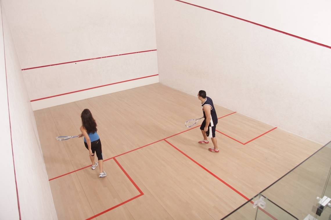 Zwei Leute spielen Squash in einem Innenraum mit roten Linien auf dem Boden.