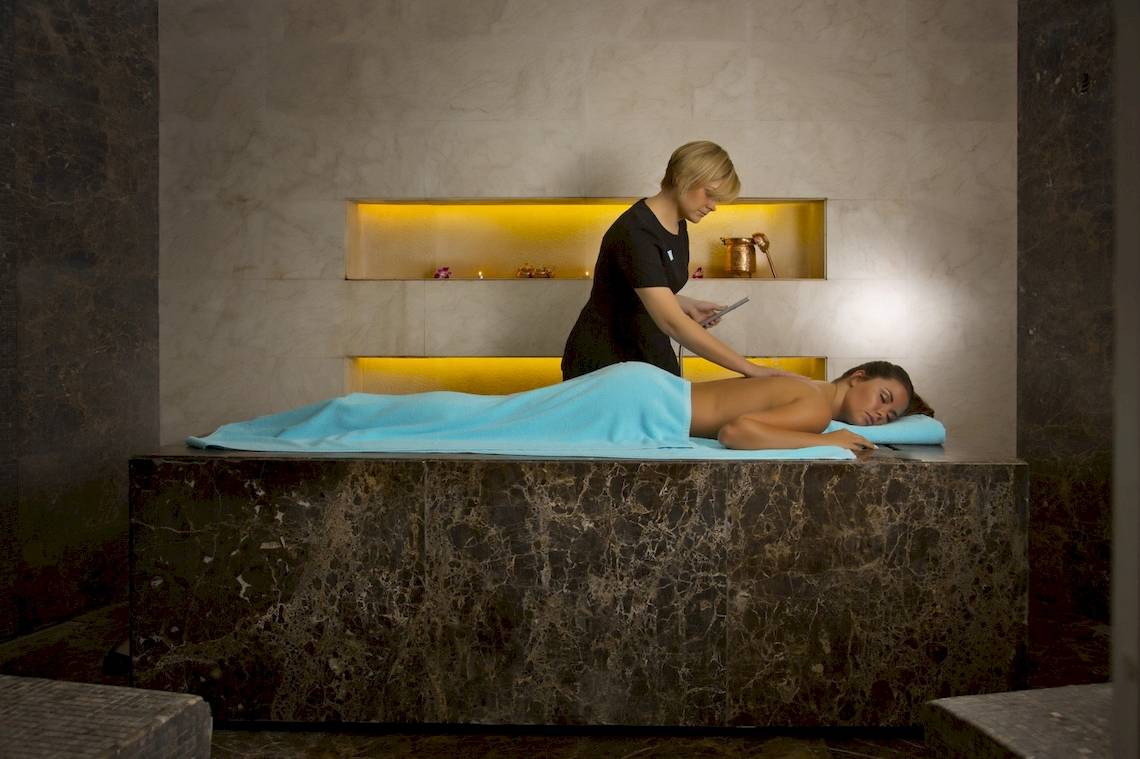 Massage im Al Ain Rotana Hotel mit einer Frau, die sich entspannt auf einem Marmorbett befindet.