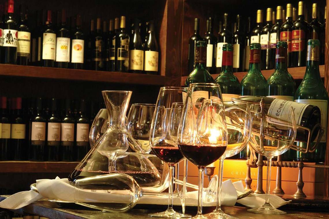 Weinflaschen im Weinkeller mit gefüllten Kelchen und Weinkaraffen