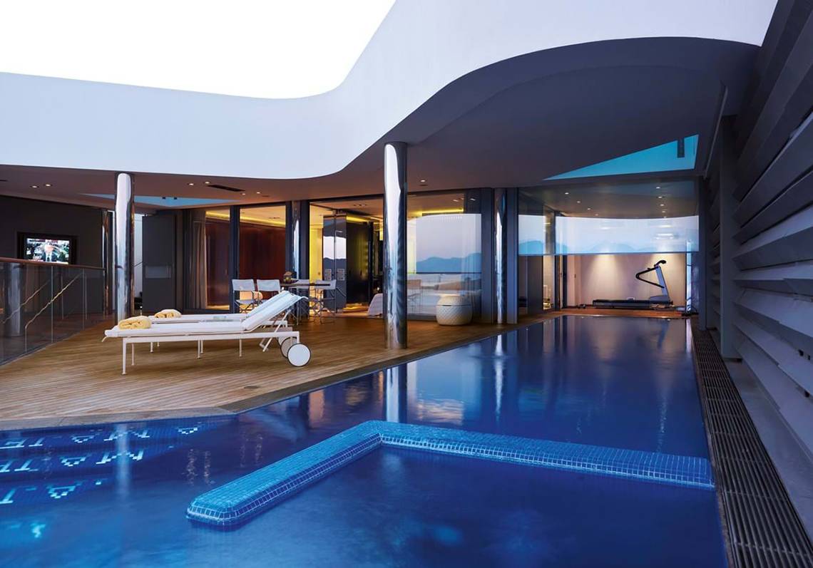 Innenpool des Elounda Beach Hotel mit Loungebereich und Fitnessgeräten.