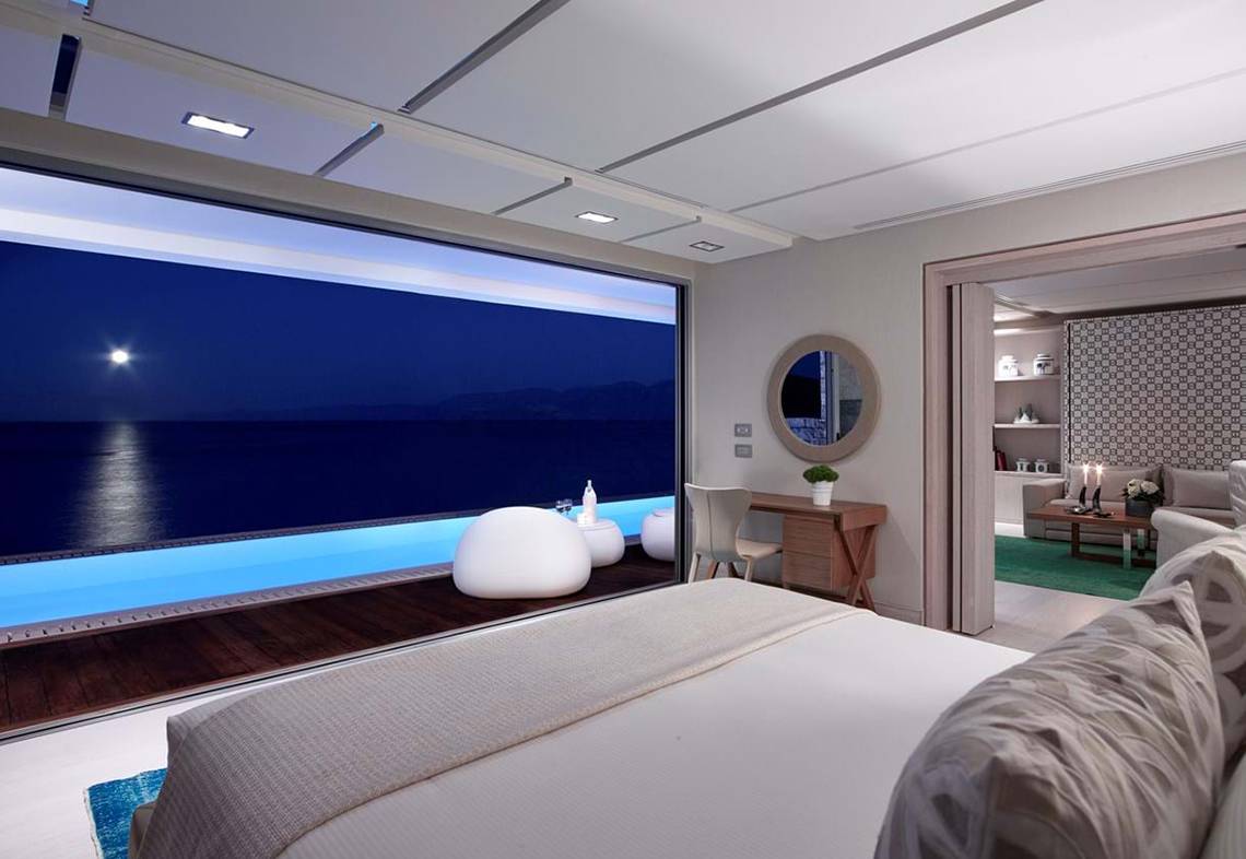 Schlafzimmer im Elounda Beach Hotel & Villas mit Meerblick und beleuchtetem Pool.