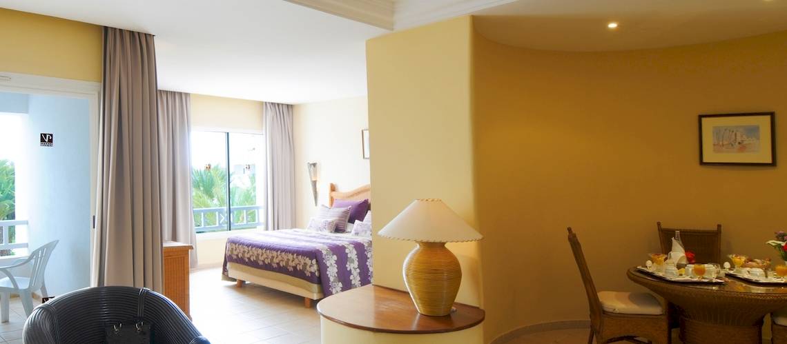 Innenansicht eines Zimmers im Djerba Resort Hotel mit Bett, Tisch und Lampe.