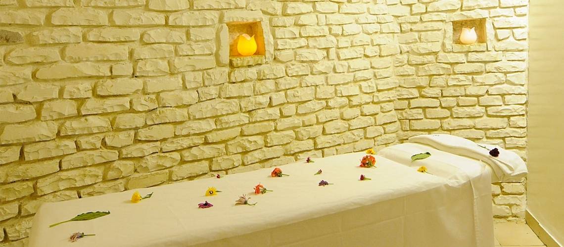 Massageraum im Djerba Resort mit weißen Steinwänden, zwei eingelassenen Kerzen und einem Massagetisch mit Blumen