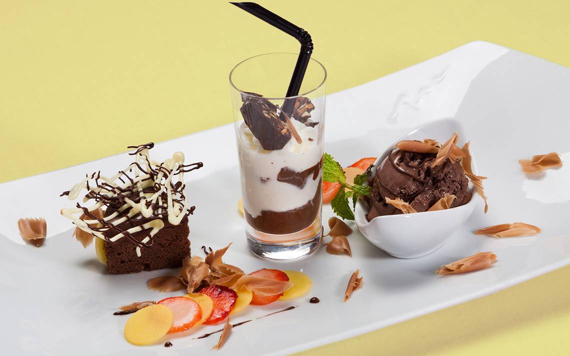 Ein weißer Teller mit einem Brownie, einem Glas mit Schokoladengetränk und Eiscreme sowie einem Eiskübel.