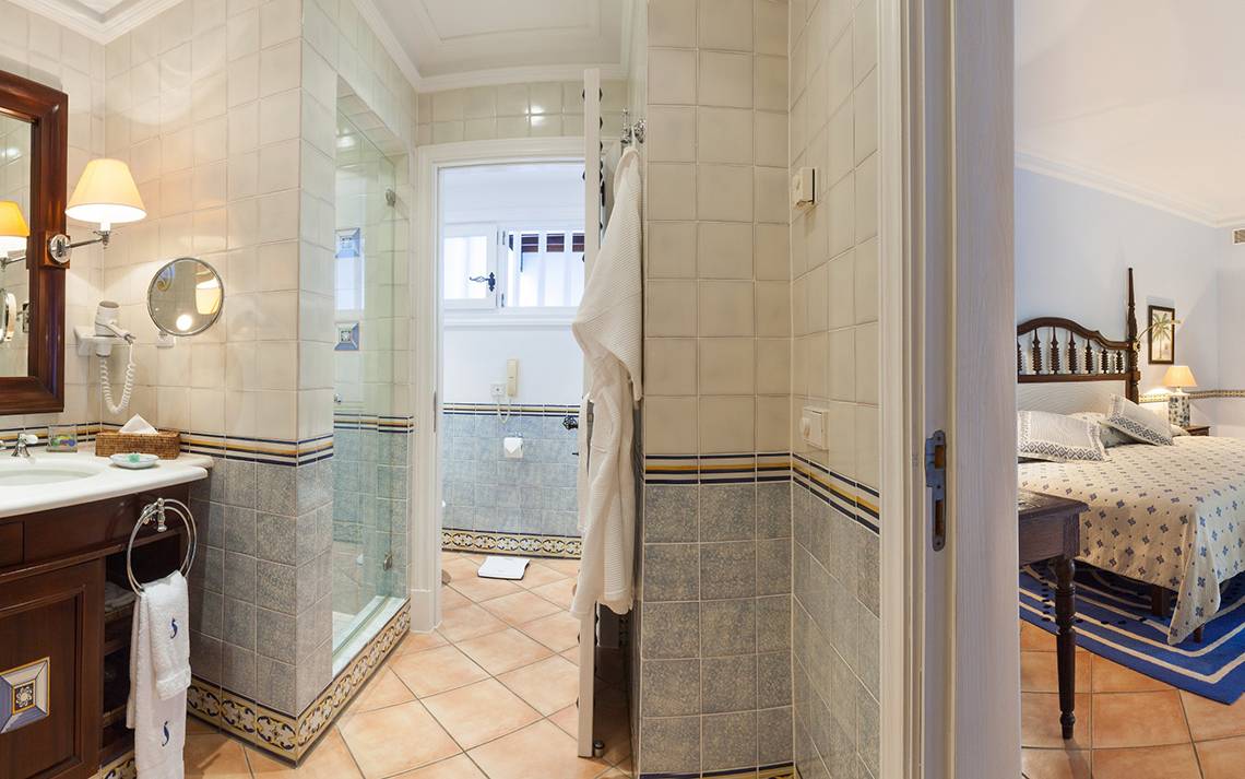 Badezimmer und Schlafzimmer im Seaside Grand Hotel Residencia mit blauen Fliesen und einem Bett.