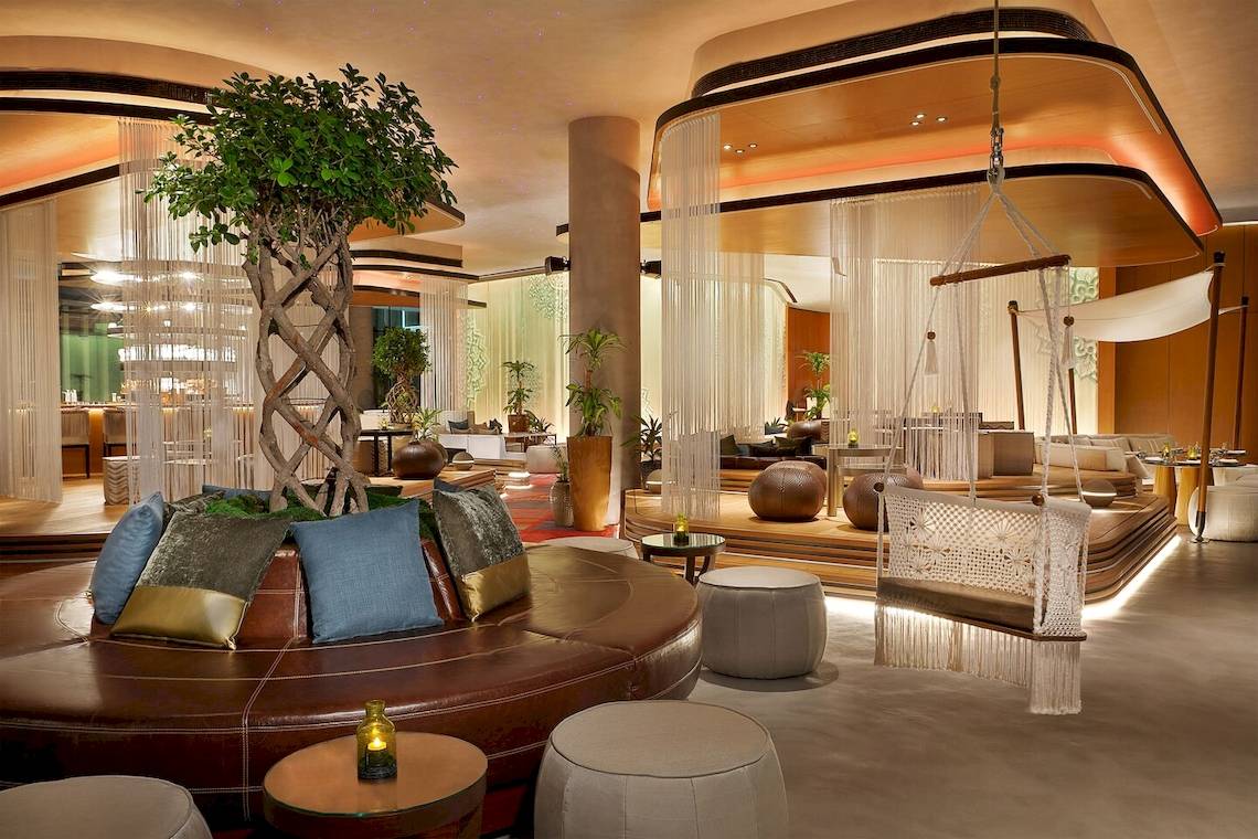 Lobby des W Muscat Hotels mit zentralem Baum, braunem Sofa und Hängesessel.