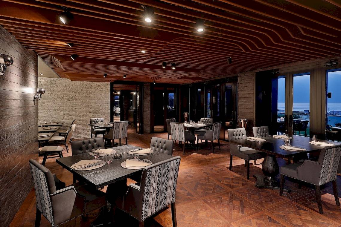 W Muscat Hotel Innenraum Restaurant mit Holzboden, gepolsterten Stühlen und Tischen.