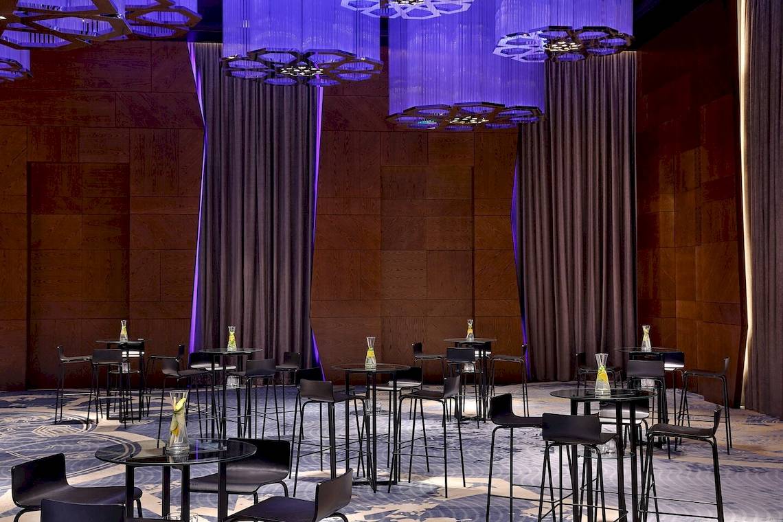 W Muscat Hotel Barbereich mit violetten Kronleuchtern und dunklen Möbeln.