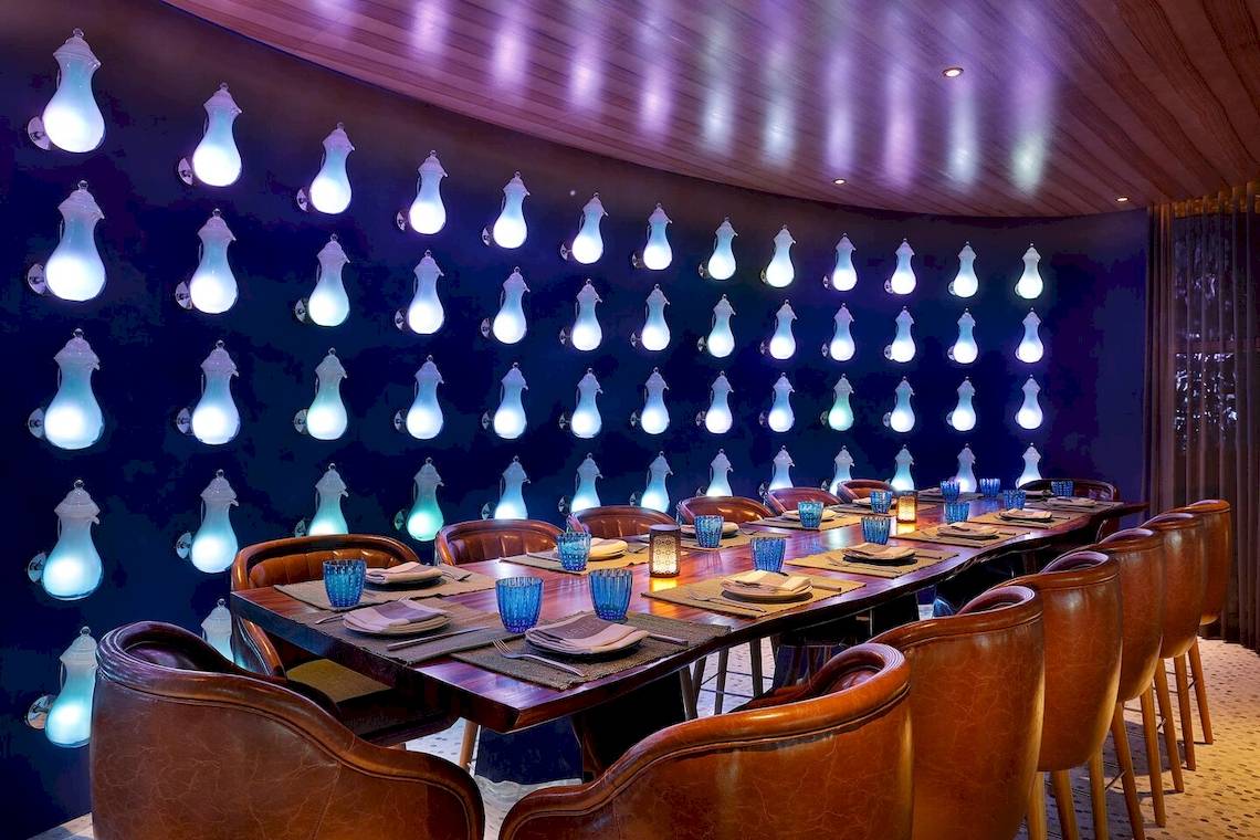Restaurant im W Muscat Hotel mit langer Tafel und blauer Wandbeleuchtung.