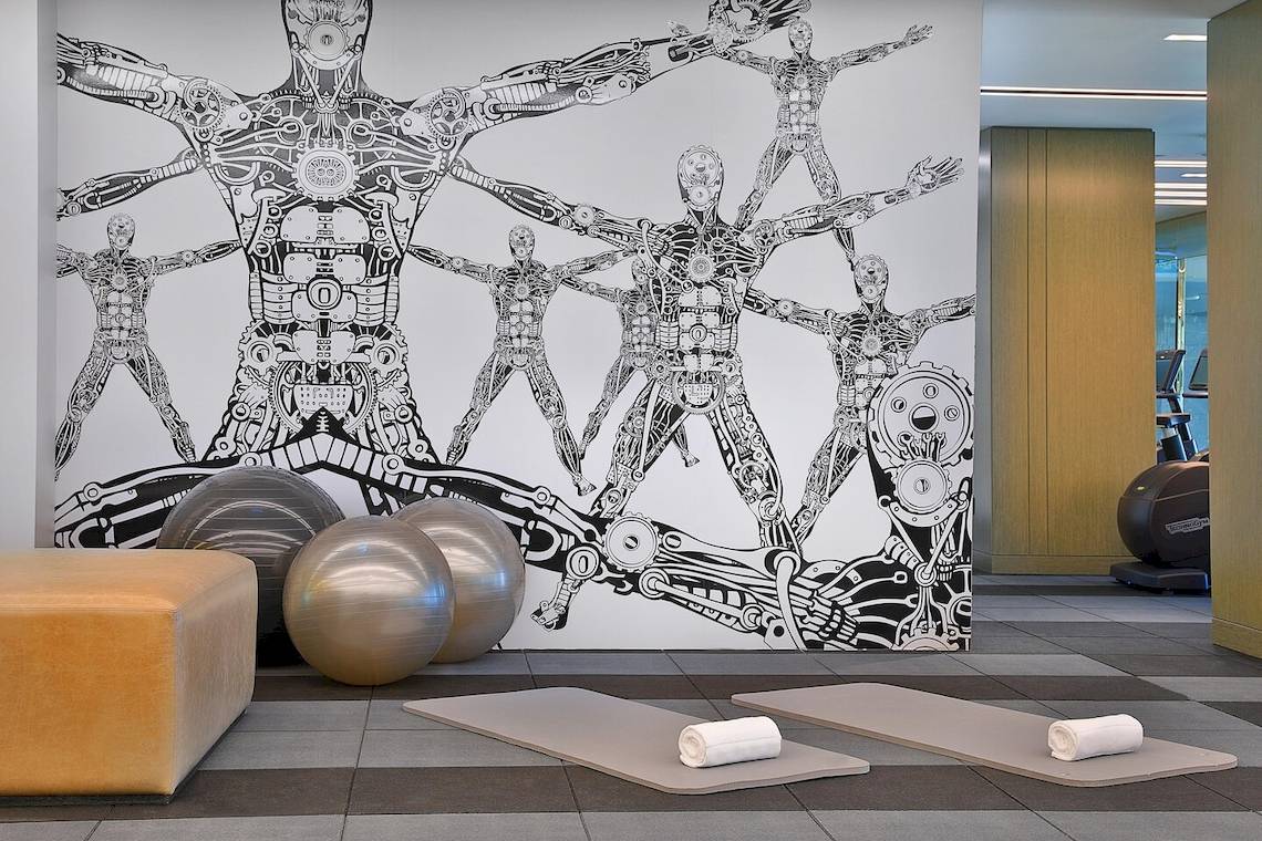 Fitnessraum im W Muscat Hotel mit einer Wandgestaltung von menschlichen Figuren und Fitnessgeräten.