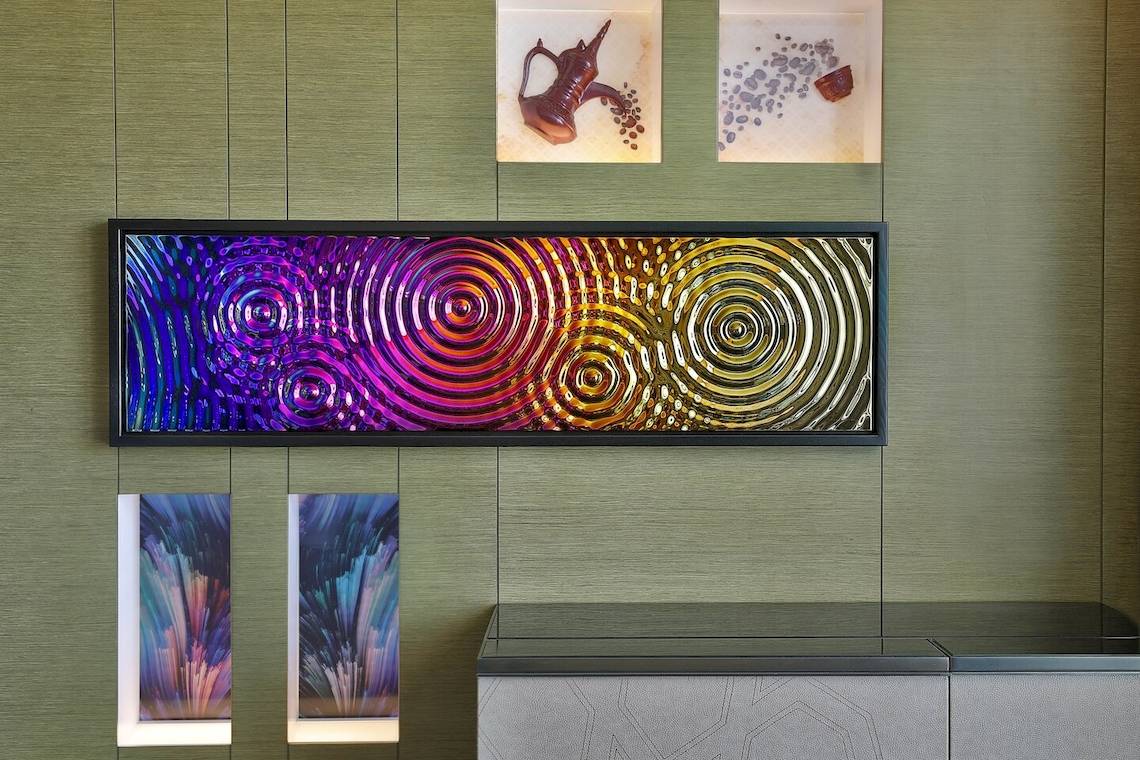 Kunstwerke an der Wand im W Muscat Hotel, darunter ein großes zentrales Gemälde und zwei kleinere neben der Rezeption.