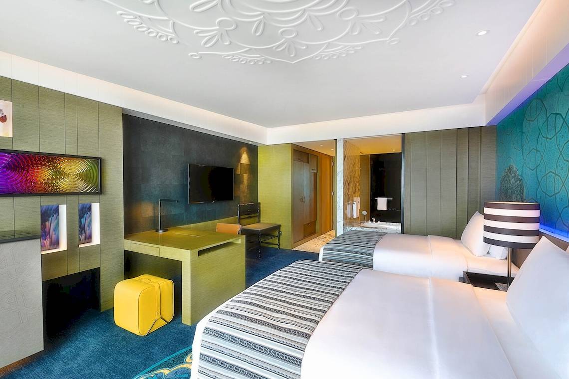 Schlafzimmer im W Muscat Hotel mit zwei Betten, Arbeitsbereich und modernen Einrichtungselementen.