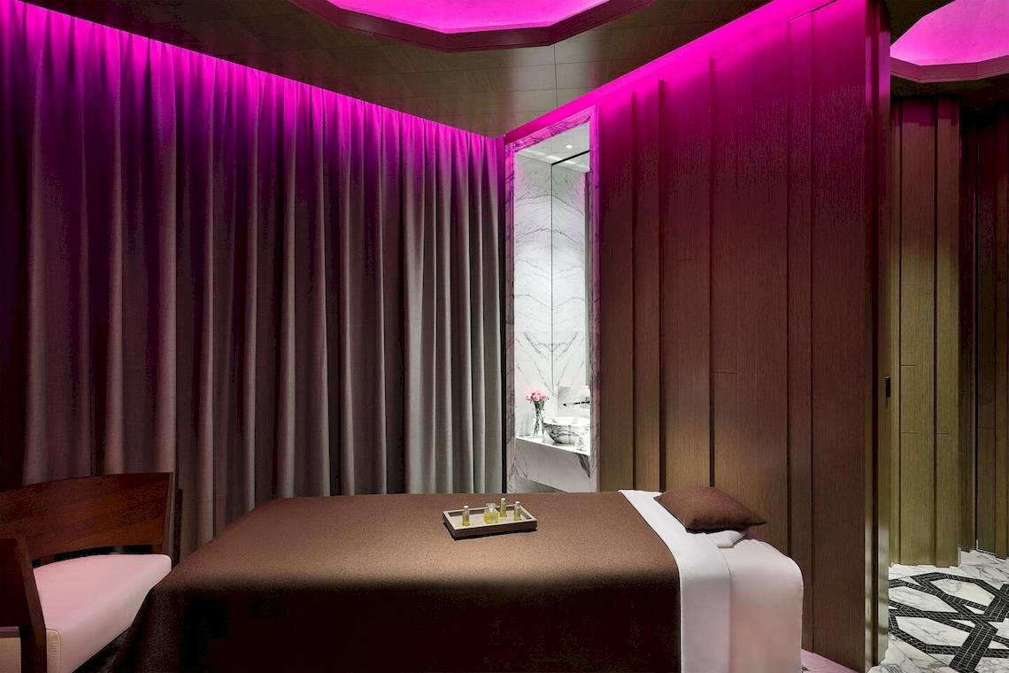 Behandlungsraum im W Muscat Spa mit violetten Lichtern und einem Massagebett.