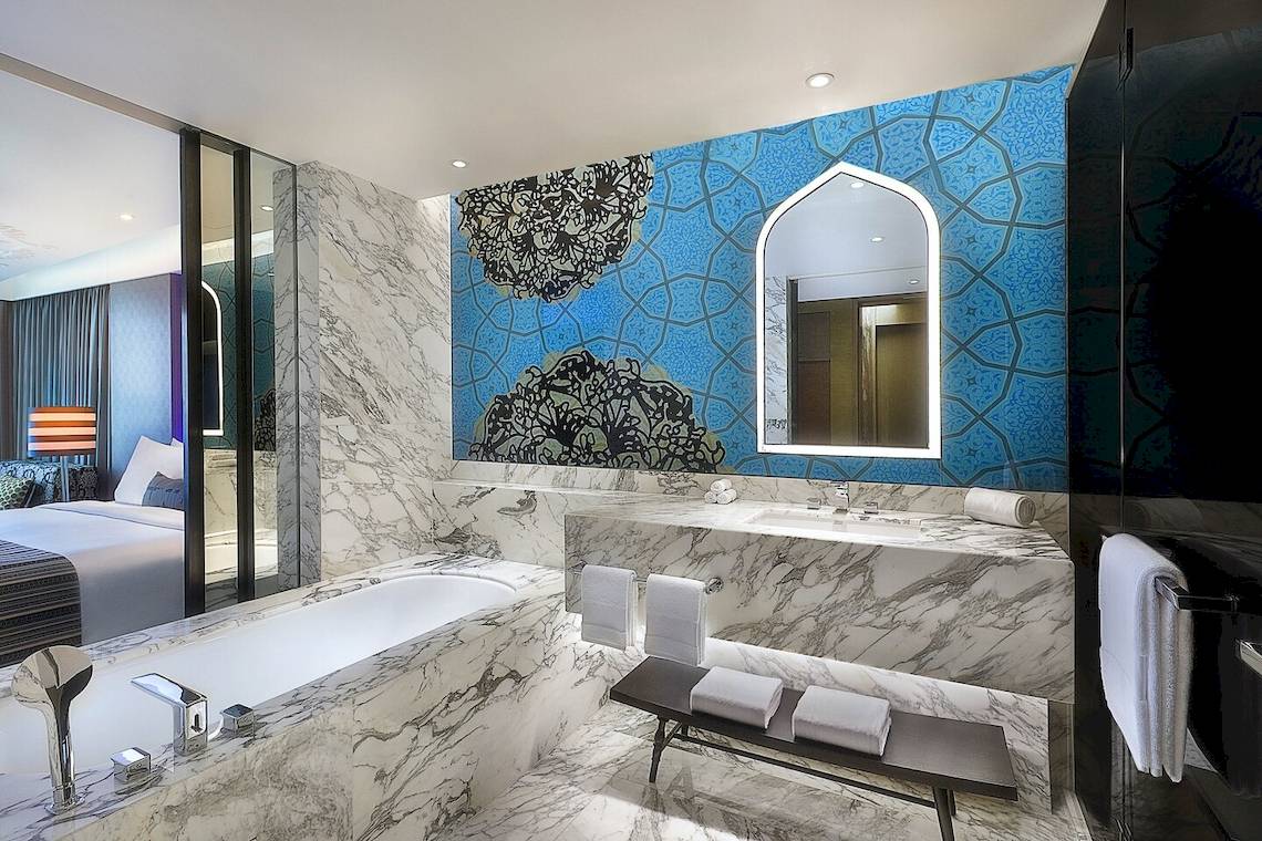 Badezimmer im W Muscat Hotel mit Marmorwänden, blauen Wandmustern und einer Badewanne.