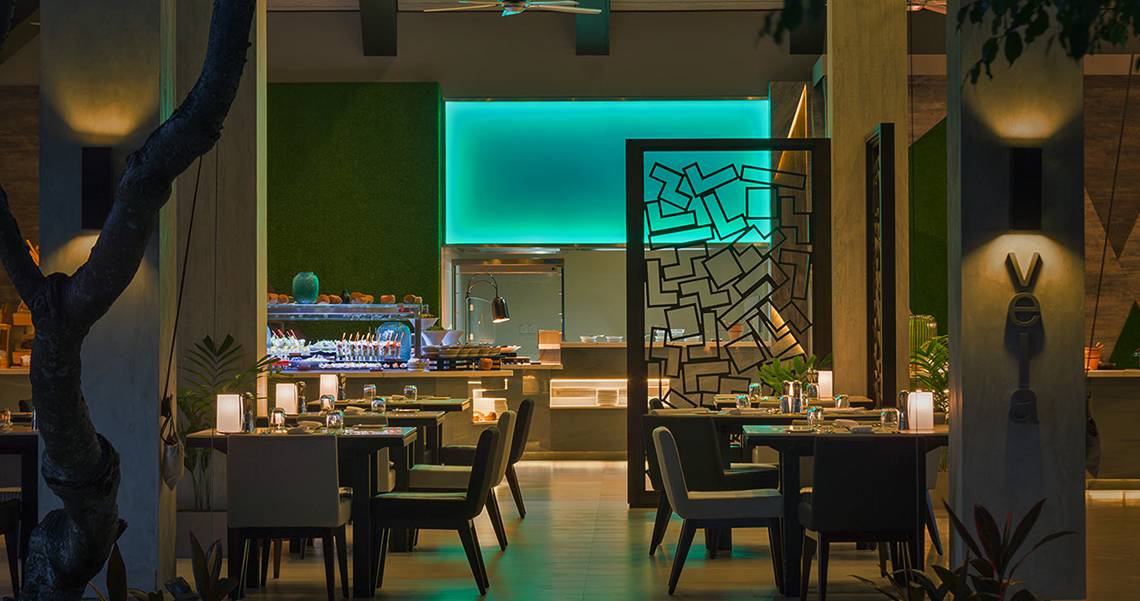 Innenbereich des Restaurants im Velassaru Maldives Hotel mit blau beleuchteter Wand und gedeckten Tischen.