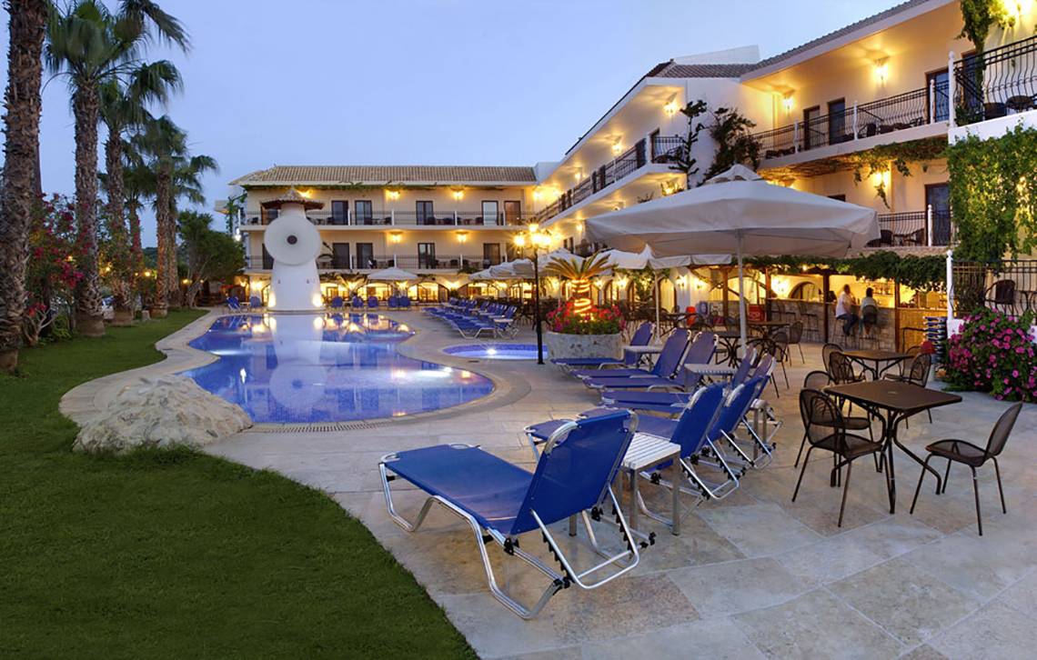 Pool-Lounge-Bereich des Almyrida Beach Hotels bei Nacht mit blauen Liegestühlen und Schirmen.