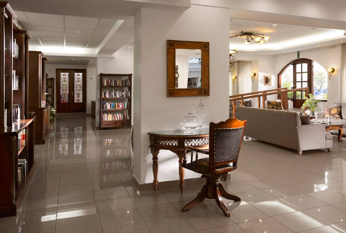 Innenansicht der Lobby des Almyrida Beach Hotels mit Bücherregal, Tisch und Sofa.