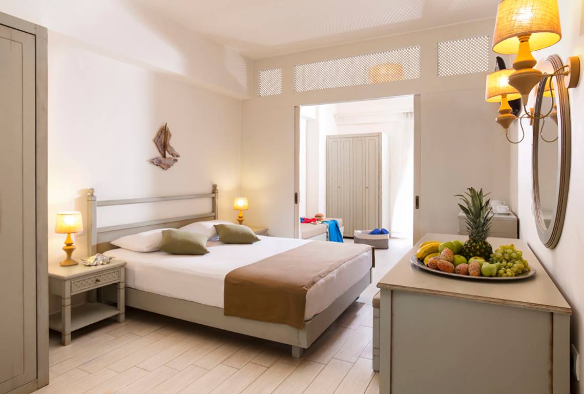 Innenansicht eines Schlafzimmers im Almyrida Beach Hotel mit Bett, Nachttischen und Obstplatte.