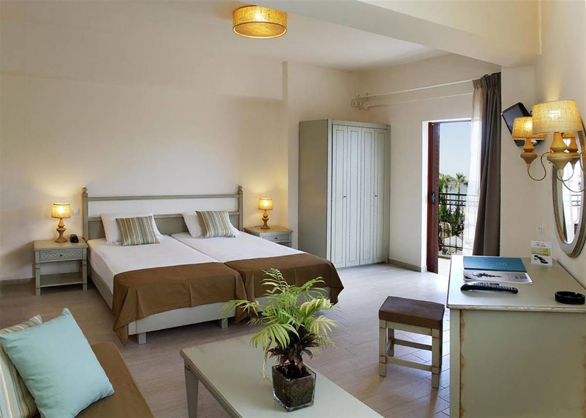 Schlafzimmer im Almyrida Beach Hotel mit zwei Betten, Nachttischen, Deckenlampen und einem Kleiderschrank.
