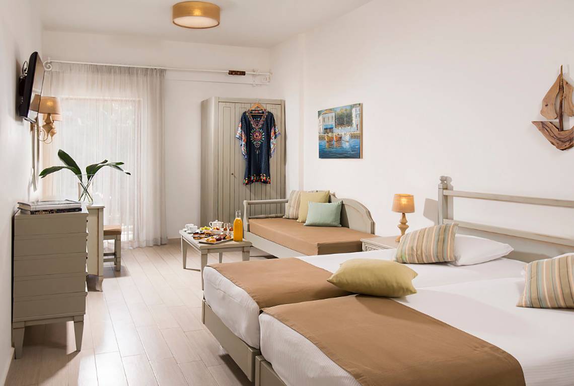 Doppelzimmer im Almyrida Beach Hotel mit zwei Betten, Nachttischen, einem Schrank, einem Sofa und einem Fenster.