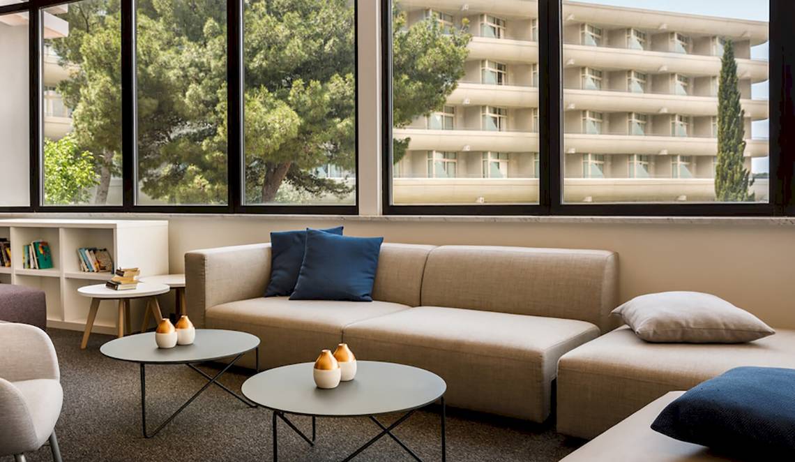 Remisens Hotel Albatros Lobby mit Sofas, Tischen und Büchern in der Nähe eines Fensters.