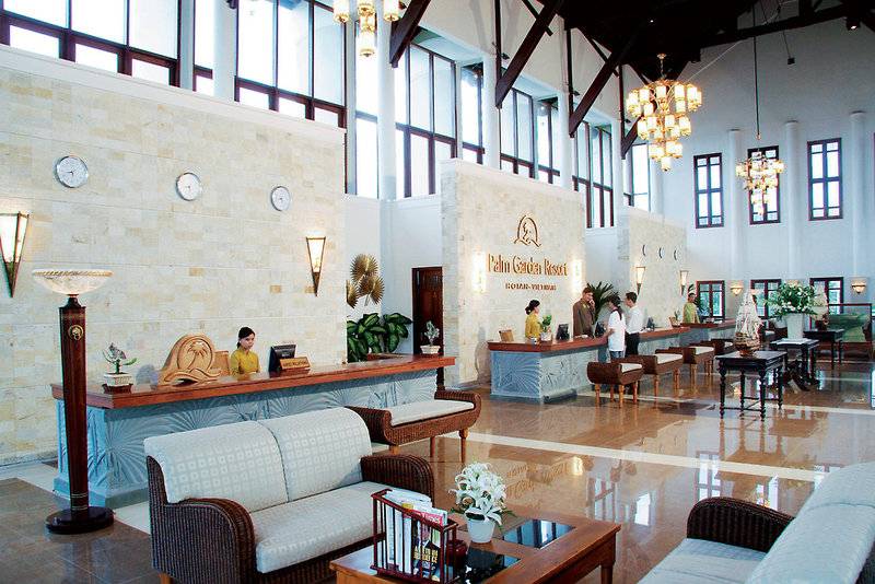 Lobby des Palm Garden Beach Resort in Hoi An mit Rezeptionstresen, Sofas und Deckenleuchten.