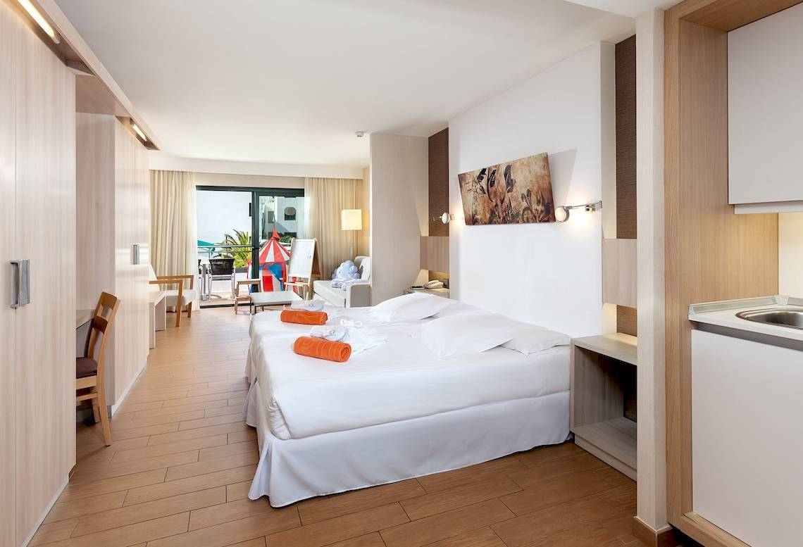Doppelbett mit weißen Laken und orangenen Handtüchern im Schlafzimmer des Be Live Experience Lanzarote Beach Hotels.