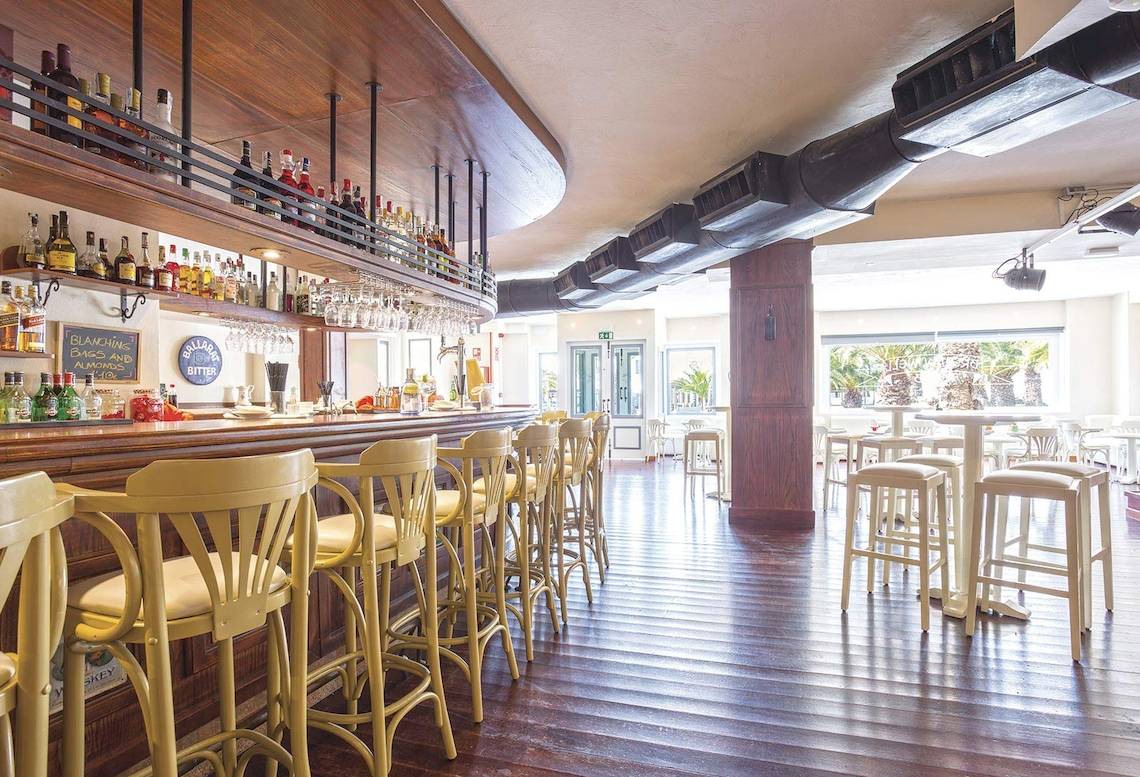 Bar im Be Live Experience Lanzarote Beach Hotel mit gelben Stühlen und einer Theke mit Flaschen.
