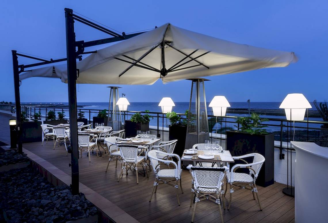 Außenterrasse des Be Live Experience Lanzarote Beach Hotels bei Nacht mit Tischen und Stühlen unter einem großen Schirm.