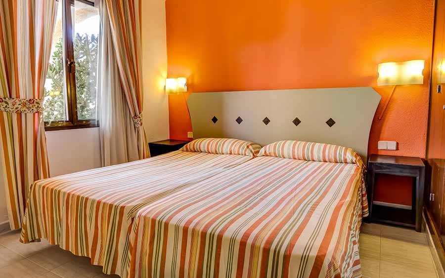 Doppelbett im Hotelzimmer im SBH Taro Beach mit orangefarbenen Wänden und gestreiften Bettdecken.
