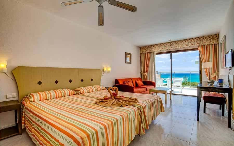 Hotelzimmer mit Meerblick, Bett, Couch, Tisch und Balkon.