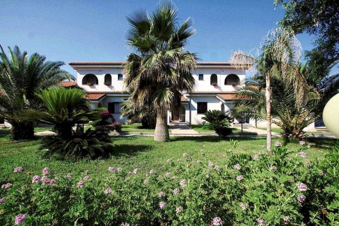 Außenansicht des Villaggio Torre Ruffa Robinson Hotels mit einer grünen Rasenfläche und Palmen.