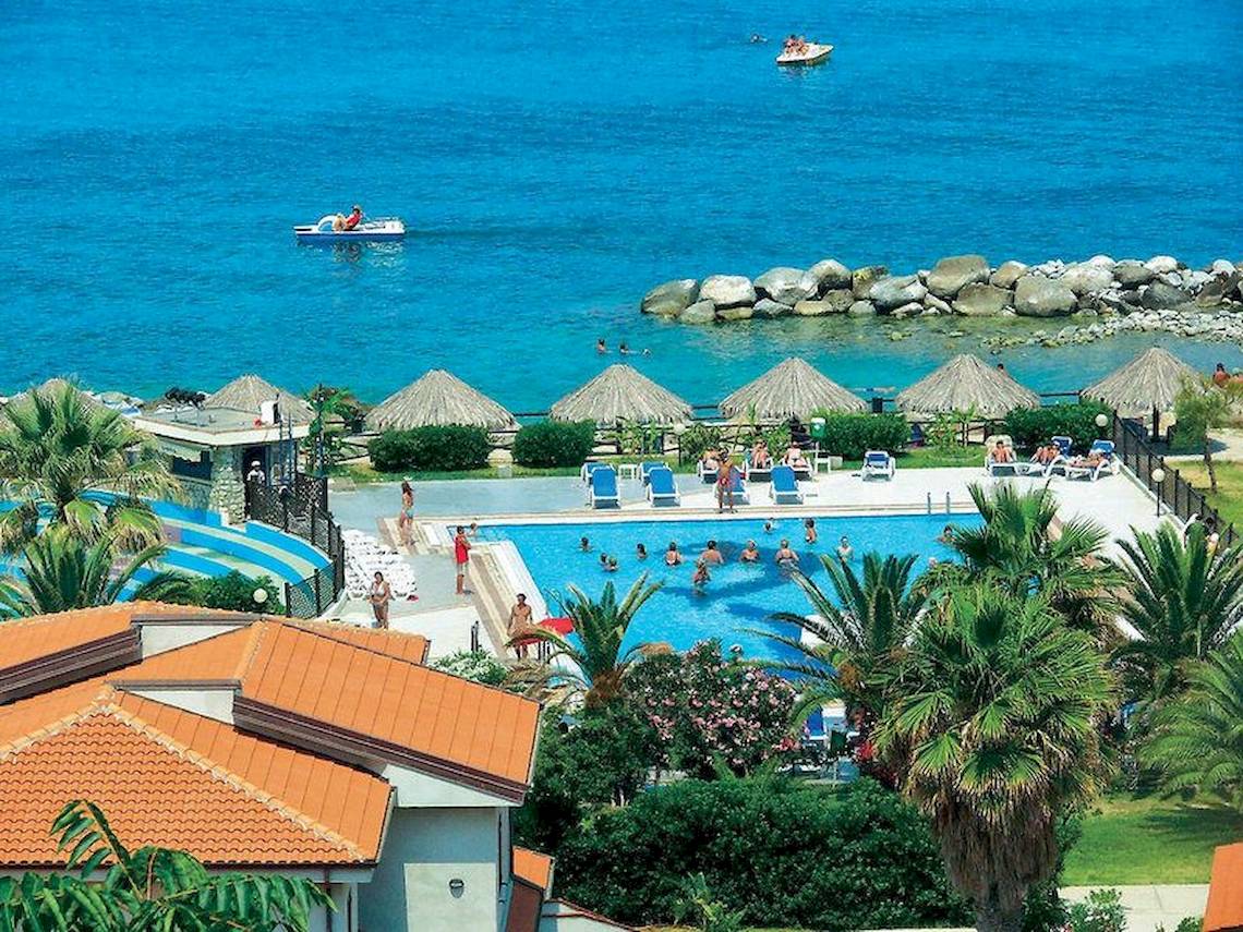 Luftaufnahme des Poolbereichs im Villaggio Torre Ruffa Robinson Hotel mit vielen Gästen und Palmen.