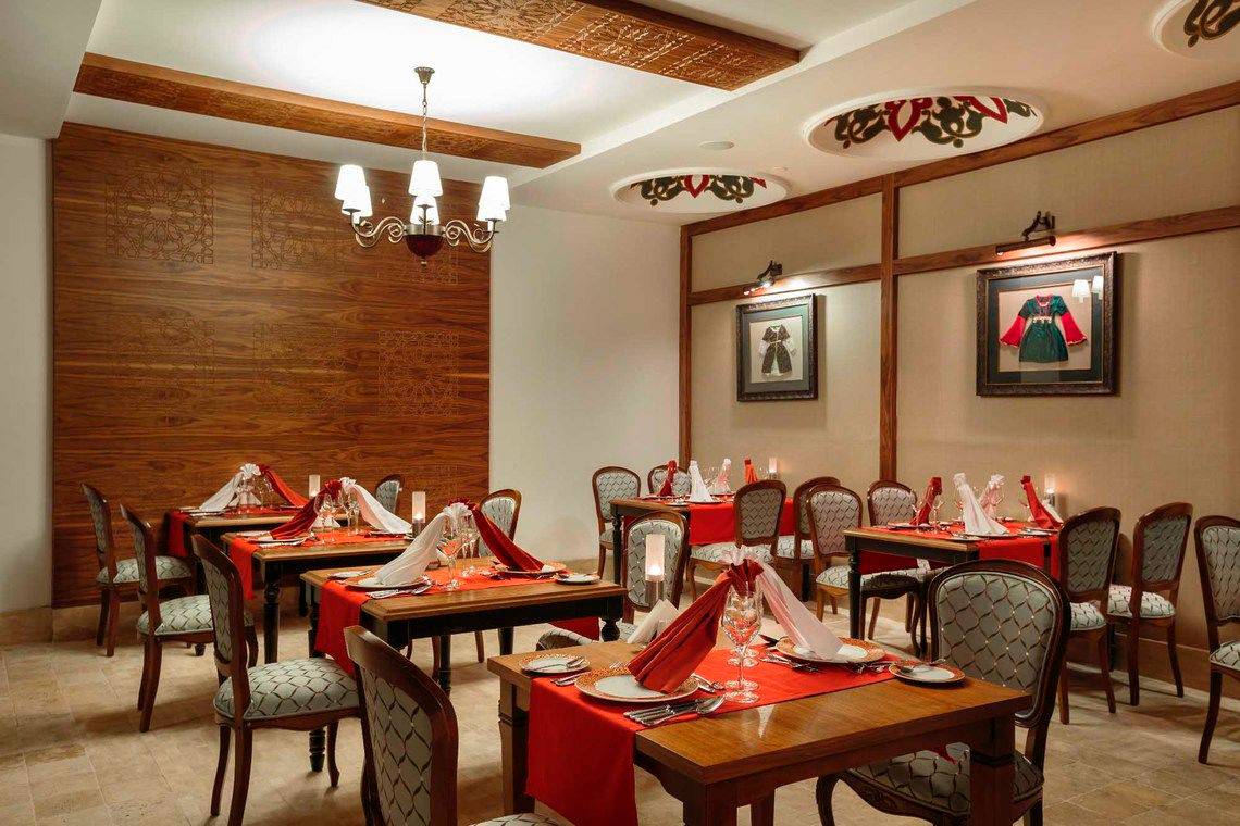 Innenansicht des Restaurants im Side Crown Palace Hotel mit dekorierten Tischen und Stühlen, Holzwänden und Deckenleuchten.