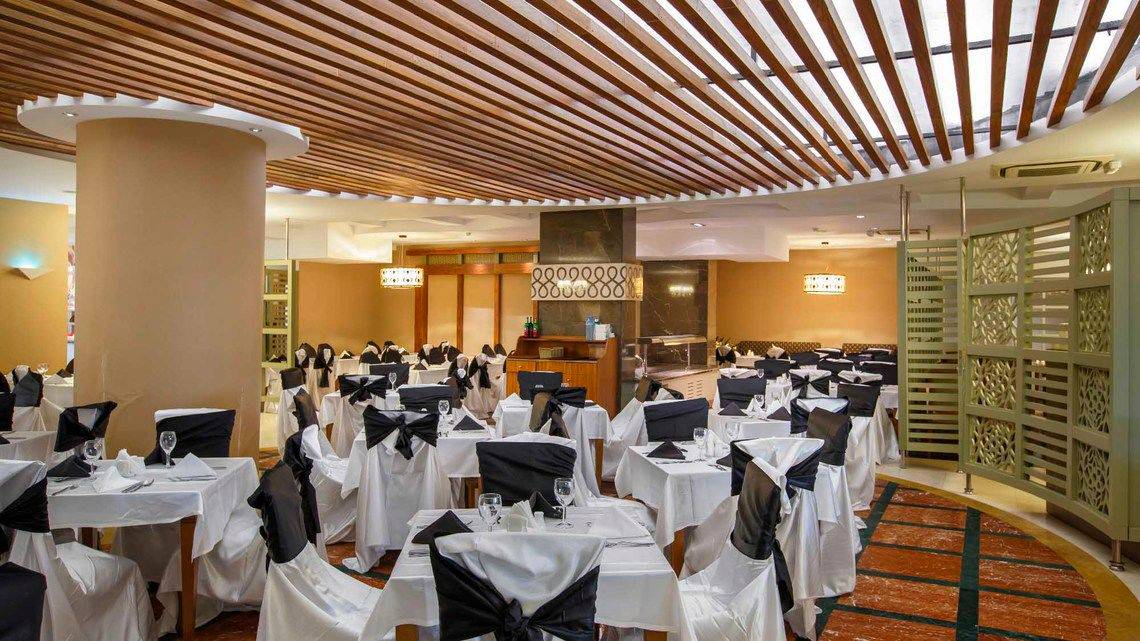 Das elegante Restaurant des Side Crown Palace mit gedeckten Tischen und hängenden Vorhängen.