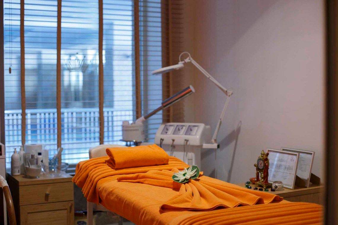 Behandlungszimmer im Side Crown Palace Hotel mit einem Massagetisch, orangenen Handtüchern und einer weißen Lotusblume.