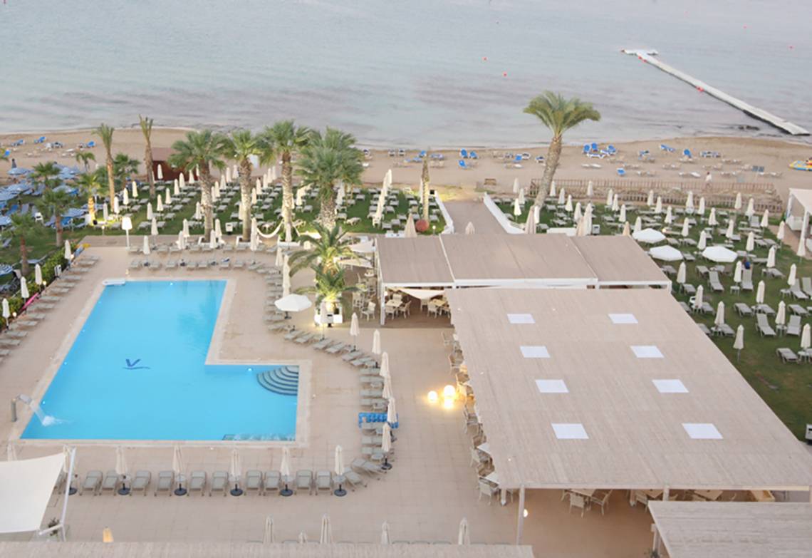 Luftaufnahme des Vrissiana Beach Hotels mit Pool, Liegestühlen und Gebäuden am Strand