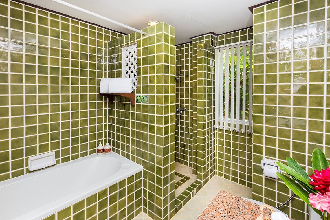 Badezimmer mit grünen Fliesen, Badewanne, Dusche und Toilettenpapierhalter.