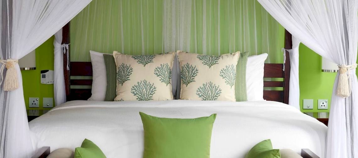 Schlafzimmer im Hilton Seychelles Northolme Resort & Spa mit grünen Wänden und weißen Vorhängen.