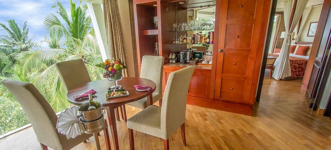 Innenansicht eines Hotelzimmers mit Esstisch, Obstschale und Weinflasche.