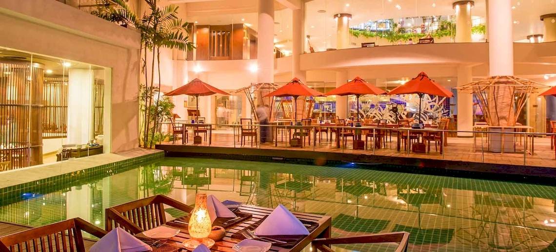 Pool-Lounge im Occidental Eden Beruwala Hotel mit roten Sonnenschirmen und Tischen.