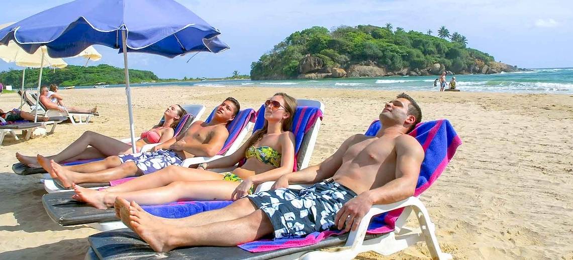 Mehrere Gäste liegen auf Sonnenliegen am Strand des Occidental Eden Beruwala.
