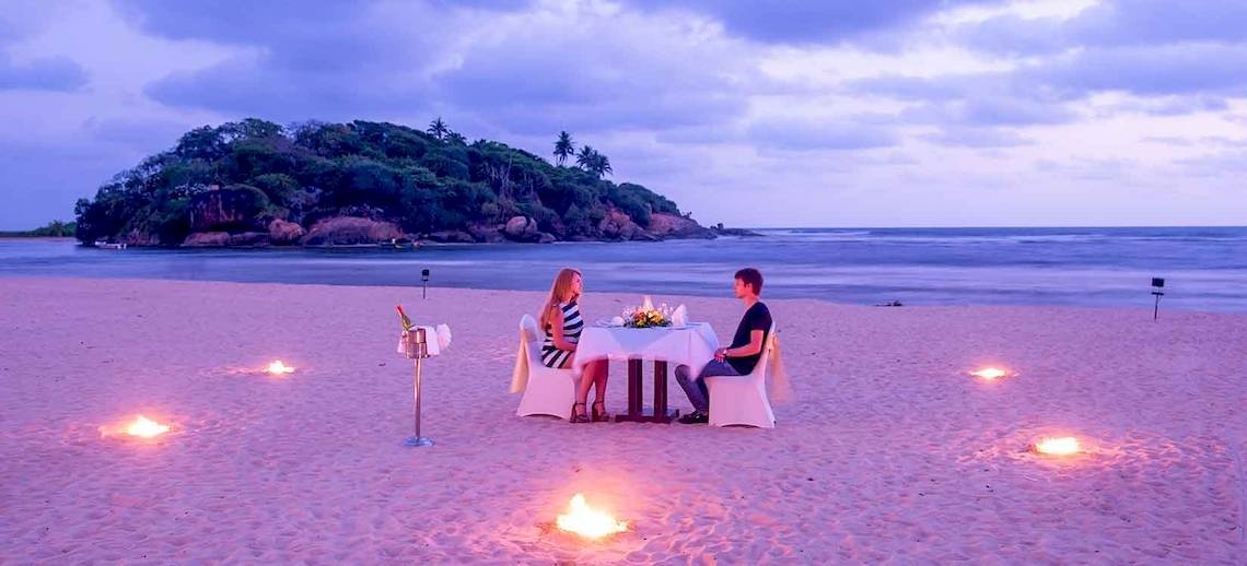 Ein Paar sitzt bei Kerzenschein am Tisch auf dem Strand des Occidental Eden Beruwala.