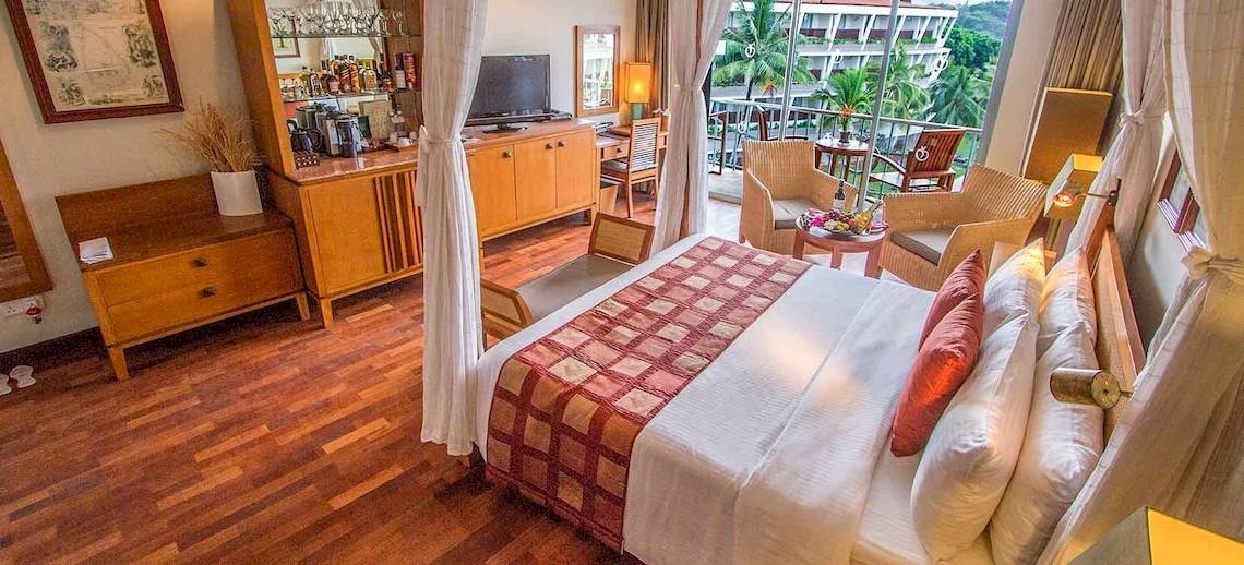 Ein elegantes Hotelzimmer im Occidental Eden Beruwala mit einem großen Bett, Holzmöbeln und einer Aussicht auf den Garten.