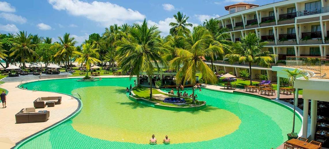 Außenansicht des Occidental Eden Beruwala Resorts mit Swimmingpool, Palmen und Hotelgebäuden.