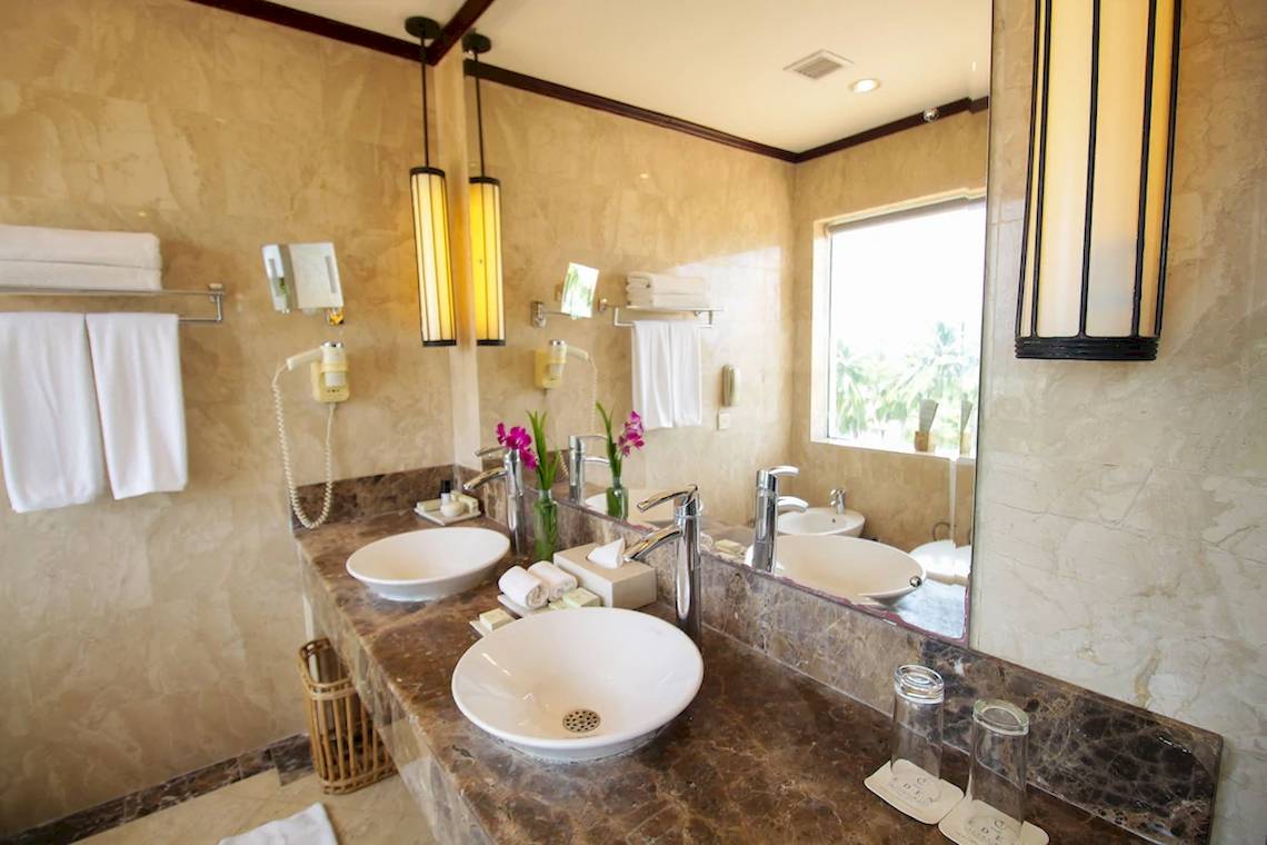 Ein Badezimmer im Occidental Eden Beruwala Hotel mit zwei Waschbecken, Spiegeln und beleuchteten Lampen.