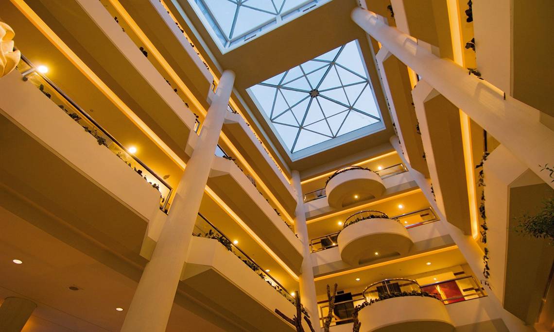 Innenansicht der Lobby des Mediterranean Beach Hotel in Zypern mit Glasdach und mehreren Stockwerken.
