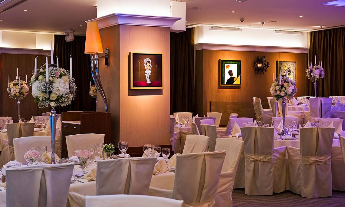 Bankettsaal im Mediterranean Beach Hotel mit gedeckten Tischen und Gemälden an der Wand.